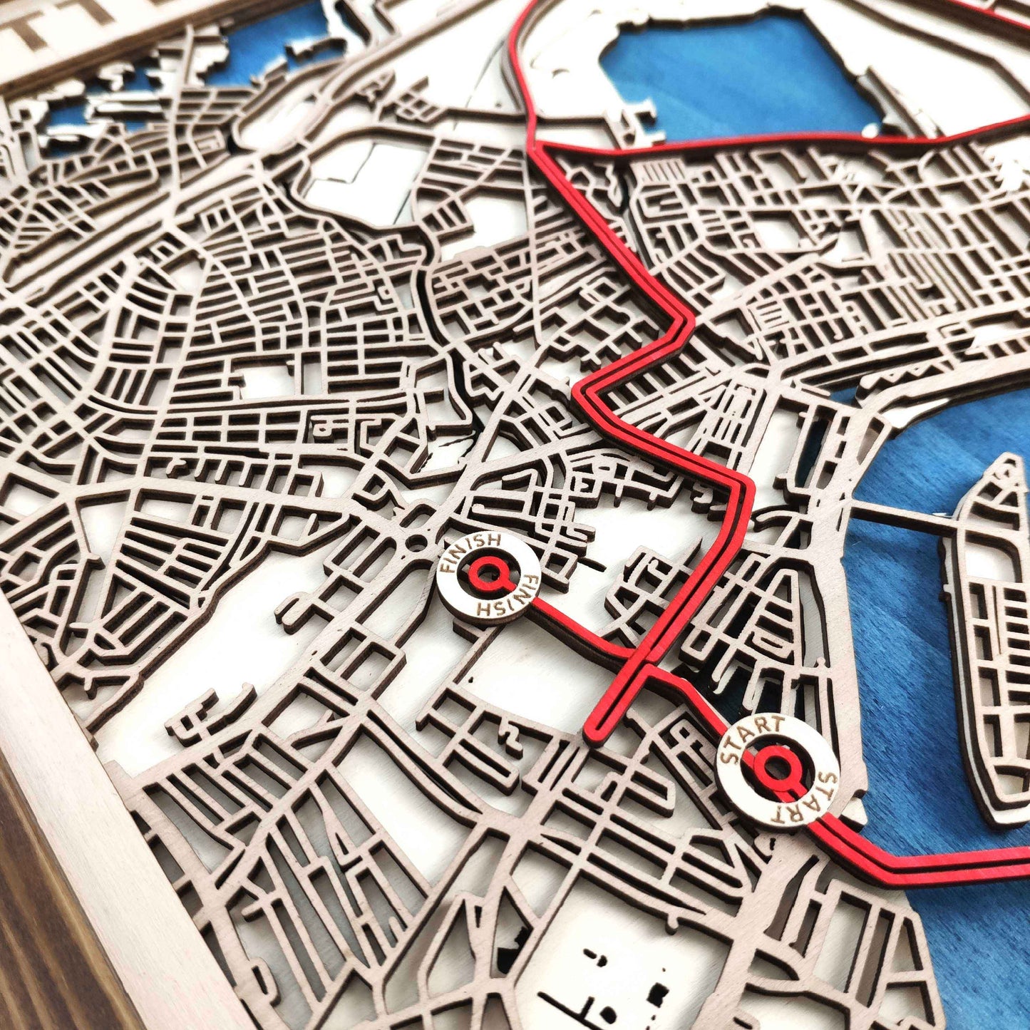Multi-layered wooden map of a city with a red route highlighting a "Start" and "Finish" location.