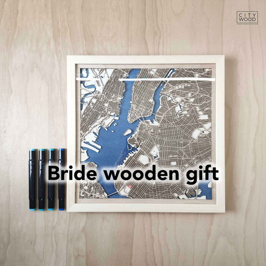 A framed wooden map of New York City is displayed on a wooden surface with four blue-tipped markers.