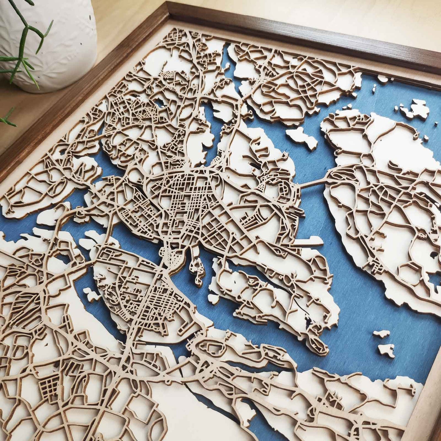 Laser-cut wooden layers of a 3D city map, water, land, and street grid, stacked together